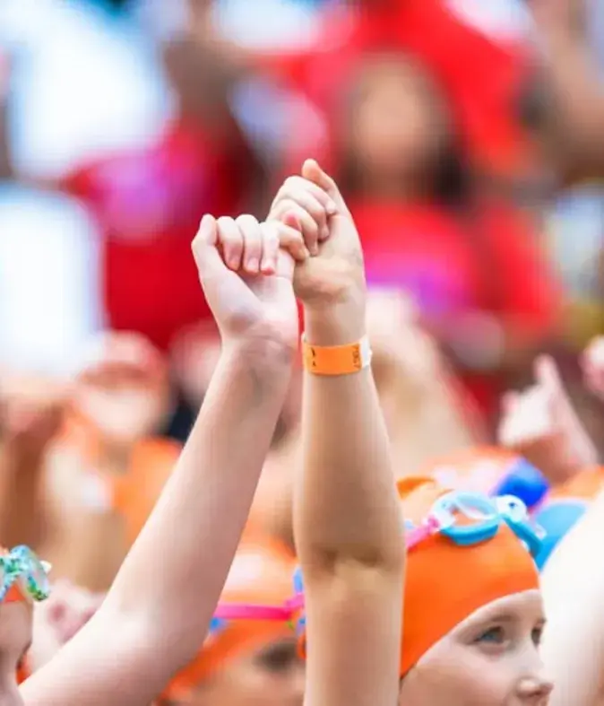 Children in orange swim caps raising linked pinkies at a Pinky Swear event